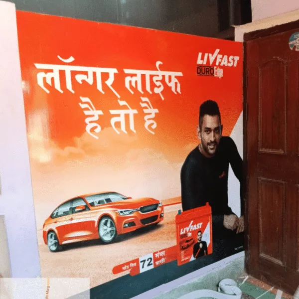 Outdoor advertising agency-designed Livfast battery wall branding with celebrity endorsement and vibrant orange car graphic.